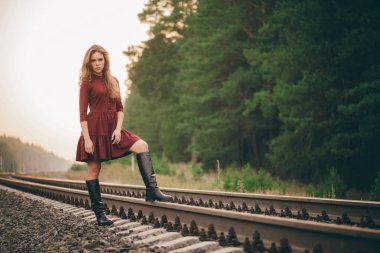Demiryolu üzerinde ormanda doğada kıvırcık doğal saçları ile Güzel üzgün düşünceli kız. Bordo elbiseli hayalperest bayan demiryolunda yürüyor. Şafakta rayların üstünde ki depresif kız. Sonbaharda saçta güneş. Kötü ruh hali.