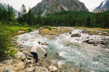 Dağ Nehri boyunca yol üzerinde gezgin. Vahşi dağ deresinde hızlı su akıntısı. Dere, zengin bitki örtüsü, orman ile Highland manzara. Dağ turizmi. Turist derede su ısıtıcısı doldurur. Vahşi doğaya.