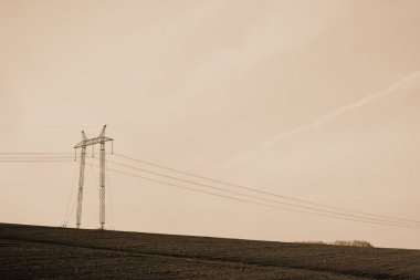 Sepya tonlarında gökyüzünün altında alan da güç hatları ile atmosferik manzara. Fotokopi alanı ile elektrik kulesi arka plan görüntüsü. Yerden yüksek voltajlı kablolar. Tek renkli elektrik endüstrisi.