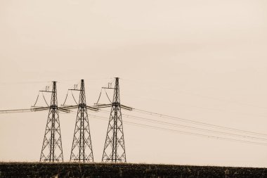 Gökyüzü yakın çekim arka planda güç hatları. Sepya tonlarında kopya alanı ile elektrik direği silueti. Yerden yüksek voltajlı kablolar. Tek renkli elektrik endüstrisi.