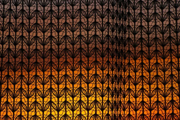 Wonderful vivid dawn from window through patterned curtain. Amazing warm sky behind silhouettes of tulle texture. Orange sunlight. Cosiness textured colorful background with sunrise. Copy space.