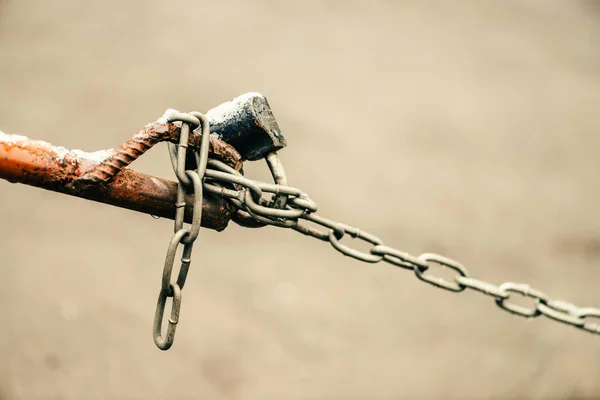 Closed padlock on chain of brown fence is close-up on background of asphalt with bokeh with copy space. Backdrop with lock of parking place. Warm image of checkpoint.