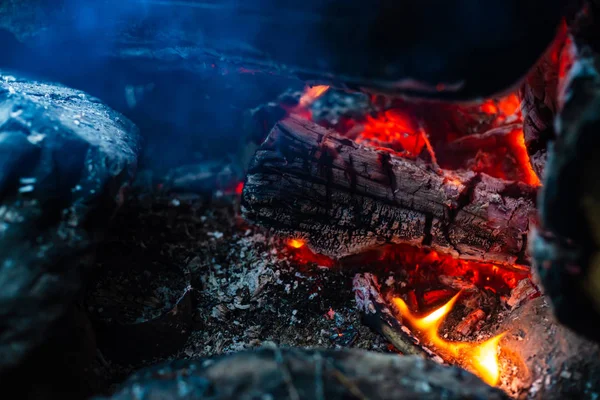 くすんだ丸太は鮮やかな火で焼かれた キャンプファイヤーのオレンジ色の炎と大気の背景 コピースペースで内部からたき火の想像を絶する詳細な画像 煙と灰がクローズアップ — ストック写真