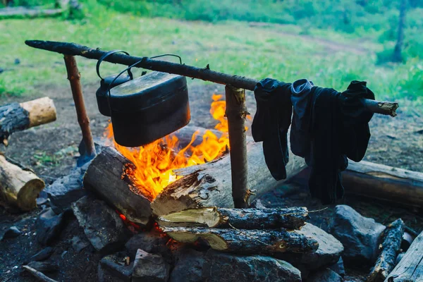 Drying wet clothing on the bonfire during camping. Socks drying on fire. Cauldron and kettle above campfire. Cooking of food on nature. Firewood and branches in fire. Active rest in forest.