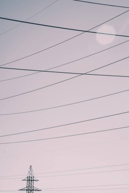 Güneş ışığında gökyüzünün arka planında yüksek voltaj kabloları olan iletiler. Gökyüzünde fotokopi alanı olan birçok kablonun tek renkli arkaplan görüntüsü. Güç hatları soluk tonlarda.