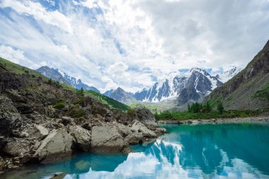 Dağ gölü dev güzel buzul önünde büyük taşlar ve kayalar ile çevrilidir. İnanılmaz karlı dağlar. Kar lı sırt. Yaylaların görkemli doğasının harika atmosferik manzarası.