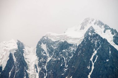 İnanılmaz büyük bir buzul tepesi. Bulutlu gökyüzünde karlı dağ sırası. Sis içinde kar ile harika dev kayalık sırt. Yaylaların görkemli doğasının atmosferik minimalist manzarası. Sakin dağ manzarası.