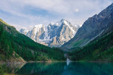 Muhteşem, dev, karlı dağlar. Nehir buzuldan dağ gölüne akar. Dağlık bölgelerdeki suda yansıma. Tepede beyaz kar var. Muhteşem atmosferik Altai doğası..
