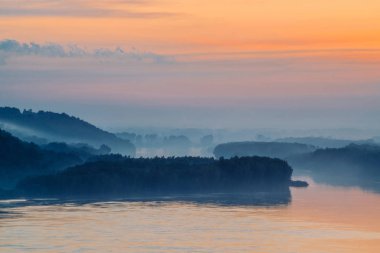 Nehrin geniş vadisinin üzerinde sabah mistik pus. Gökyüzünde şafaktan itibaren altın parlıyor. Sisin altında orman olan nehir kıyısı. Güneş ışığı gün doğumunda suya yansır. Görkemli doğanın renkli atmosferik manzara.