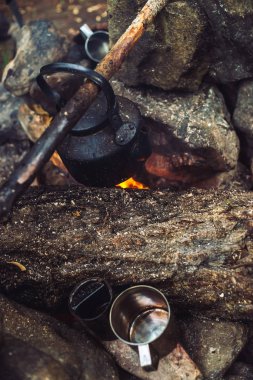 Büyük odun ile şenlik ateşinde su ısıtıcısı çay kaynatma. Açık havada çay içmek. Aktif açık hava rekreasyon. Gün batımında kamp. Doğada alacakaranlık romantik sıcak atmosfer. Aktif istirahat. Metal kupa.