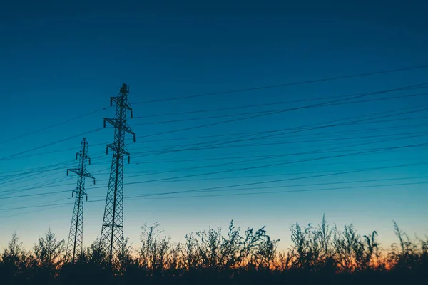 日出背景的字段中的电源线 黎明时分用电线的电线杆的剪影 暖橙色蓝天上的高压电缆 日落时分的电力行业 许多电缆在风景如画的生动的天空 — 图库照片