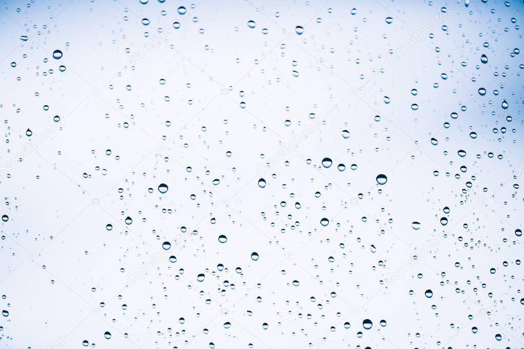 Dirty window glass with drops of rain. Atmospheric blue light background with raindrops. Droplets and stains close up. Detailed transparent texture in macro with copy space. Rainy weather.