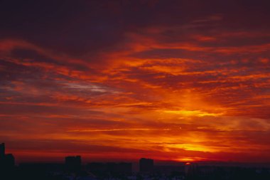 Cityscape canlı ateşli şafak ile. İnanılmaz sıcak dramatik bulutlu gökyüzü karanlık siluetleri şehir binaların yukarıda. Turuncu güneş ışığı. Gündoğumu bulutlu havalarda atmosferik arka plan. Kopya alanı.