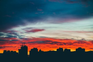 Harika varirenkli canlı şafak ile Cityscape. Şehir binalarının karanlık siluetleri üzerinde inanılmaz dramatik çok renkli bulutlu gökyüzü. Bulutlu havalarda gün doğumunun atmosferik arka planı. Kopyalama alanı.