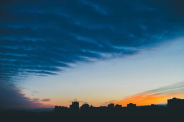 Harika varirenkli canlı şafak ile Cityscape. Şehir inşa çatıları karanlık siluetleri üzerinde Inanılmaz dramatik mavi bulut gökyüzü. Bulutlu havalarda turuncu gündoğumu atmosferik arka plan. Kopyalama alanı