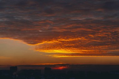 Canlı ateşli şafak ile Cityscape. Şehir bina çatıların karanlık siluetleri üzerinde Amazing sıcak dramatik bulutlu gökyüzü. Turuncu güneş ışığı. Bulutlu havalarda gün doğumunun atmosferik arka planı. Kopyalama alanı.