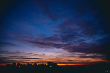 Canlı sıcak şafak ile Cityscape. Şehir binalarının karanlık siluetleri üzerinde Amazing dramatik mavi mor bulutlu gökyüzü. Turuncu güneş ışığı. Bulutlu havalarda gün doğumunun atmosferik arka planı. Kopyalama alanı.