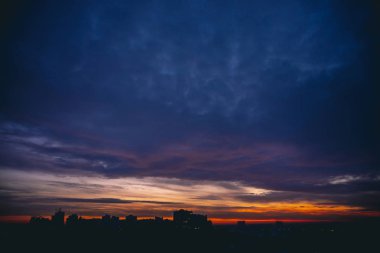 Canlı sıcak şafak ile Cityscape. Şehir binalarının karanlık siluetleri üzerinde Amazing dramatik mavi mor bulutlu gökyüzü. Turuncu güneş ışığı. Bulutlu havalarda gün doğumunun atmosferik arka planı. Kopyalama alanı.