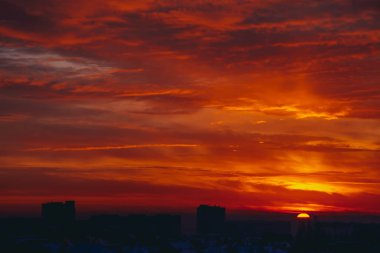 Cityscape canlı ateşli şafak ile. İnanılmaz sıcak dramatik bulutlu gökyüzü karanlık siluetleri şehir binaların yukarıda. Turuncu güneş ışığı. Gündoğumu bulutlu havalarda atmosferik arka plan. Kopya alanı.