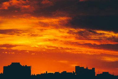 Cityscape canlı ateşli şafak ile. İnanılmaz sıcak dramatik bulutlu gökyüzü karanlık siluetleri şehir binaların yukarıda. Turuncu güneş ışığı. Gündoğumu bulutlu havalarda atmosferik arka plan. Kopya alanı.