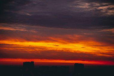 Harika varirenkli ateşli şafak ile Cityscape. İnanılmaz dramatik çok renkli bulutlu gökyüzü. Şehir binası çatılarının karanlık siluetleri. Bulutlu havalarda gün doğumunun atmosferik arka planı. Kopyalama alanı.