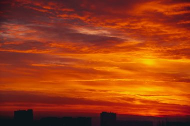 Cityscape canlı ateşli şafak ile. İnanılmaz sıcak dramatik bulutlu gökyüzü karanlık siluetleri şehir binaların yukarıda. Turuncu güneş ışığı. Gündoğumu bulutlu havalarda atmosferik arka plan. Kopya alanı.