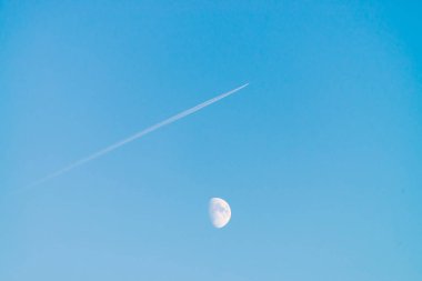 Berrak mavi gün gökyüzünde ay üzerinde jet yoğuşma izi. Minimalist mavi arka plan. Uçak çapraz olarak uçar. Uçak hava sahasında uçuyor. Gökyüzündeki beyaz ay.