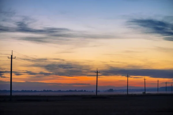 Silhouette of power lines in field on sunrise background