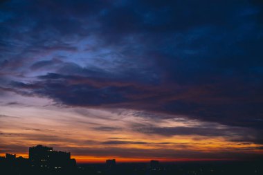 Canlı sıcak şafak ile Cityscape. Şehir binalarının karanlık siluetleri üzerinde Amazing dramatik mavi mor bulutlu gökyüzü. Turuncu güneş ışığı. Bulutlu havalarda gün doğumunun atmosferik arka planı. Kopyalama alanı.