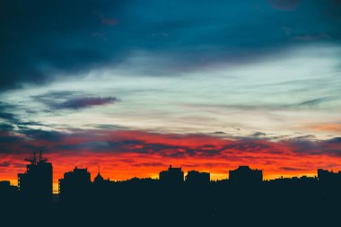Harika varirenkli canlı şafak ile Cityscape. Şehir binalarının karanlık siluetleri üzerinde inanılmaz dramatik çok renkli bulutlu gökyüzü. Bulutlu havalarda gün doğumunun atmosferik arka planı. Kopyalama alanı.