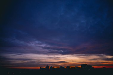 Canlı sıcak şafak ile Cityscape. Şehir binalarının karanlık siluetleri üzerinde Amazing dramatik mavi mor bulutlu gökyüzü. Turuncu güneş ışığı. Bulutlu havalarda gün doğumunun atmosferik arka planı. Kopyalama alanı.