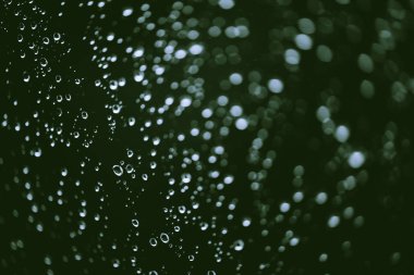 Yağmur damlalarıyla kirli pencere camı. Bokeh yağmur damlaları ile atmosferik yeşil arka plan. Damlacıklar ve lekeler kapanır. Kopyalama alanı ile makroda ayrıntılı saydam doku. Yağmurlu hava.