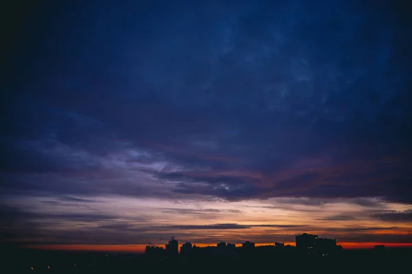 鮮やかな暖かい夜明けと都市景観 都市の建物の暗いシルエットの上に驚くべき劇的な青い紫色の曇り空 オレンジ色の日光曇りの天候の日の出の大気の背景 スペースのコピー — ストック写真