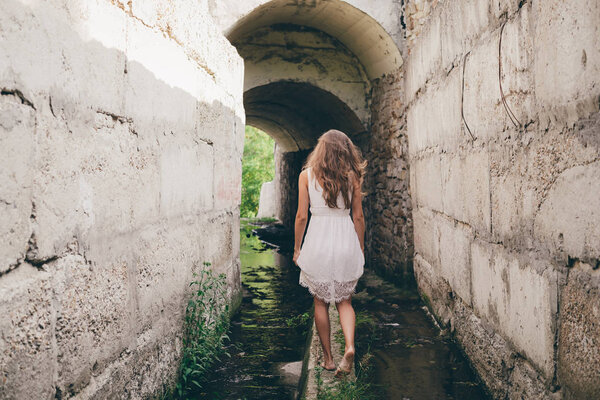 Beautiful inspired girl with curly natural hair in white dress is walking in tunnel
