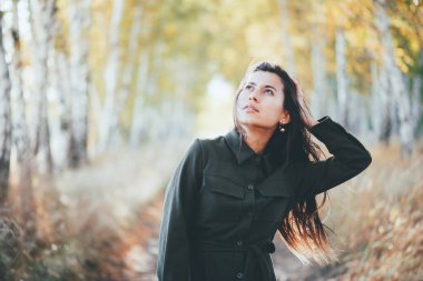 Sonbahar sarı yapraklarının arka planında uzun doğal siyah saçları olan rüya gibi güzel bir kız. İlham dolu kız sonbahar ormanlarında doğanın tadını çıkarıyor. Sonbahar coşkusu. Soluk tonlarda kadın duygusal portresi.