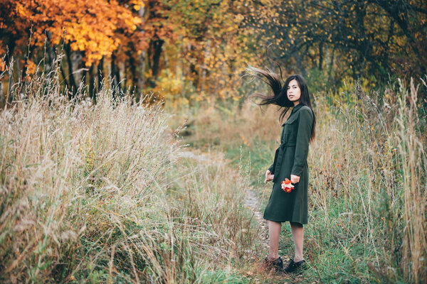 Female beauty portrait surrounded by vivid foliage. Dreamy beautiful girl with long natural black hair in full growth on background with colorful leaves. Fallen leaves in girl hands in autumn forest.