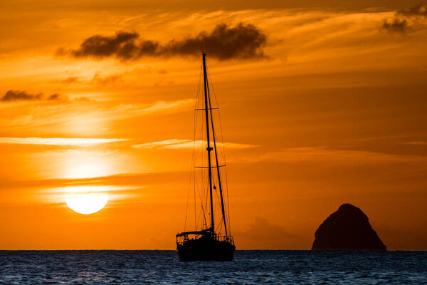 Dark silhouette of sailing boat on open sea during the sunset. The Caribbean Island Diamond rock on the horizon