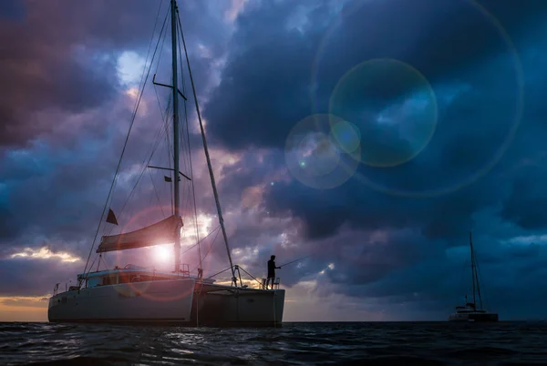 在夕阳时 双体船在公海上的黑暗轮廓与戏剧性的云 在船头钓鱼的渔夫 — 图库照片