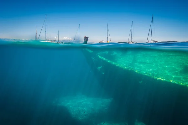 View from water line on old ship wreck and seven sailing boats anchored in close area. Sunny weather and clean water.