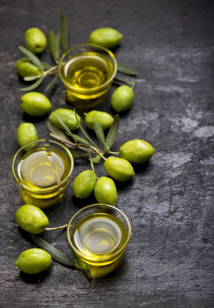 Olives vertes, branche d'olive et huile d'olive sur une planche de bois foncé — Photo