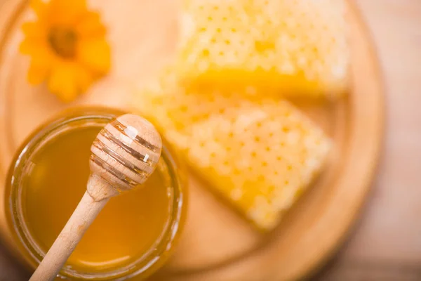 Honey dipper on the bee honeycomb background. Honey tidbit in glass jar and honeycombs wax. — Stock Photo, Image