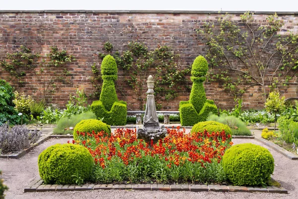 Small walled garden with topiary shrubs and red flowers.