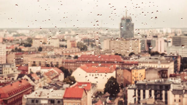 Raindrops on the dirty glass, behind the glass blurred panorama of the old bright colored city, abstract cozy retro nostalgically background