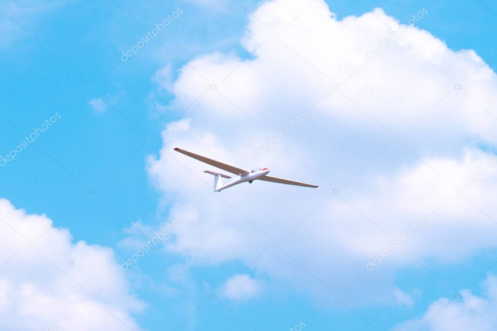 Small glider flying against the blue sky and clouds