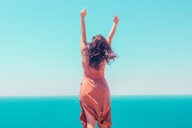 Bir yaz kahverengi elbise li, elleri yükseltilmiş genç bir kız.