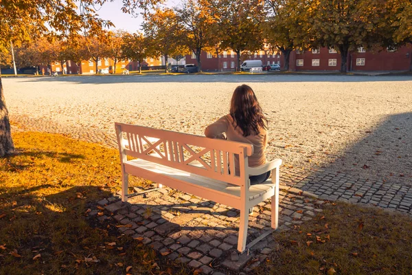 Vacker ensam flicka sitter på en vit bänk i höst Stockfoto