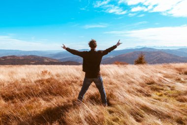 Kıvırcık saçlı, ellerini yana açmış adam eğleniyor. 