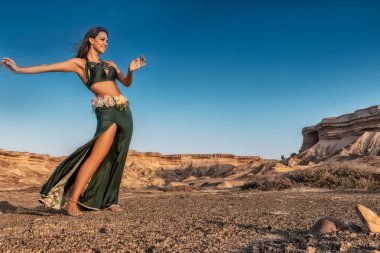 Woman dancing to the famous belly dance with natural sunset light, in the Namibe Desert with canyons. Africa. Angola. clipart