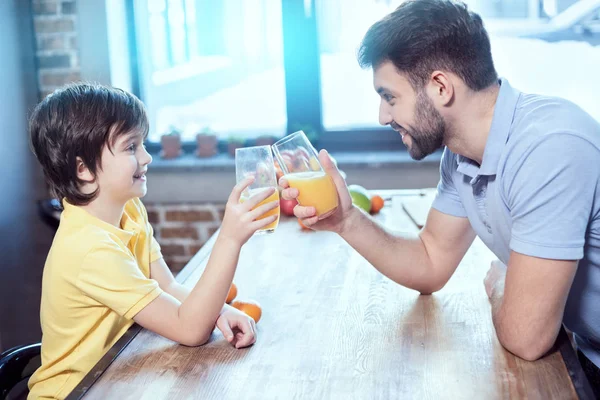 少年と彼の父親はテーブルにジュースのメガネによってチリンと笑みを浮かべてください — ストック写真