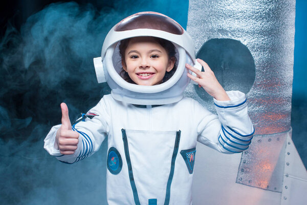smiling child in astronaut costume doing thumb up gesture 